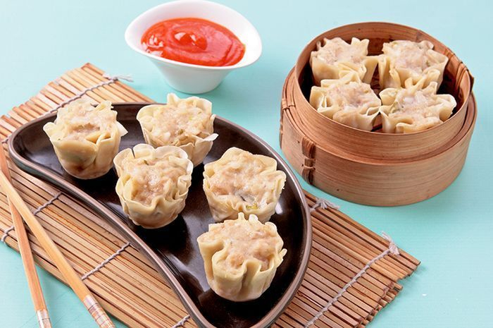 gambar dimsum, frozen food, aneka baso, siomay udang, siomay ayam. Paparan Gambar : <p>Terdapat hidangan di atas meja warna putih kebiruan. Di sebelah kiri terhidang 5 buah siomay yang disajikan di atas piring setengah bulat warna hitam yang dialasi dengan taplak tirai bambu yang artistik dan di sebelah kiri piring siomay tersebut terdapat sepasang sumpit untuk makan. Di tengah terdapat saus sambal merah yang ditempatkan dalam mangkuk saus kecil berbentuk lingkaran berwarna putih. Dan di sebelah kanan terhidah empat buah siomay dimsum yang diletakkan di atas kukusan kecil khas dimsum yang terbuat dari anyaman bambu yang sangat artistik. Sungguh hidangan yang sangat cantik, indah dan sungguh menimbulkan selera. Akhir paparan gambar.</p>