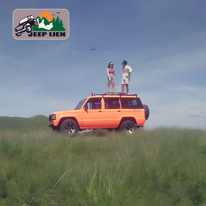 gambar sewa jeep trooper banyuwangi, jeep ijen. Paparan Gambar : <p>Terdapat 2 orang pria dan wanita berdiri di atap mobil jip troper warna oranye di tengah padang rumput yang hijau dengan latar belakang alam pegunungan.</p>